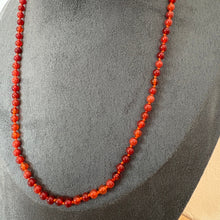 Load image into Gallery viewer, A beaded necklace made of round, polished red-orange beads draped on a dark grey fabric jewellery display bust.