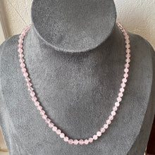 Load image into Gallery viewer, A single strand necklace made of light pink faceted beads, displayed on a grey velvet jewellery bust.
