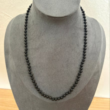 Load image into Gallery viewer, A long black beaded necklace displayed on a grey fabric jewellery bust against a light wall.
