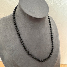 Load image into Gallery viewer, A black beaded necklace displayed on a grey fabric jewellery bust against a light textured wall.
