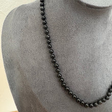 Load image into Gallery viewer, A black beaded necklace displayed on a grey fabric jewellery bust against a light wall.
