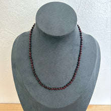 Load image into Gallery viewer, A dark red beaded necklace displayed on a grey fabric jewellery bust against a light textured wall.
