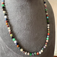 Load image into Gallery viewer, A beaded necklace made of small multicoloured polished gemstones, displayed on a grey fabric jewellery bust against a light wall.
