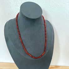 Load image into Gallery viewer, A single strand red beaded necklace displayed on a dark grey fabric jewellery bust against a white textured wall.
