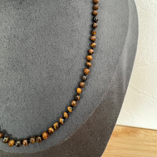 Load image into Gallery viewer, A beaded necklace made of round brown and tan tiger's eye beads, displayed on a dark grey fabric jewellery bust.
